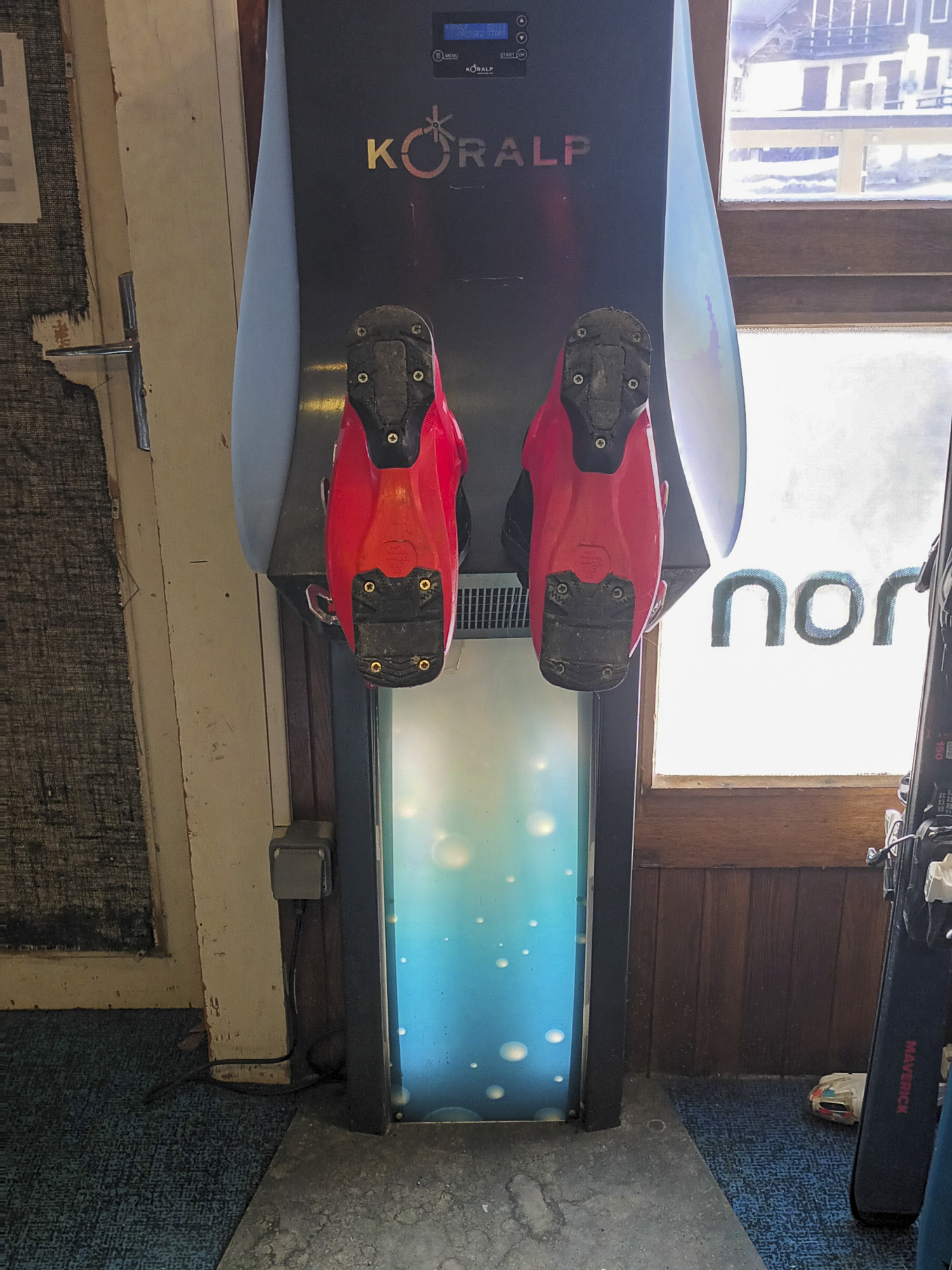 Paire de chaussures de ski Atomic rouges et noires posée à côté d'un pulvérisateur de désinfection pour matériel de sport d'hiver.